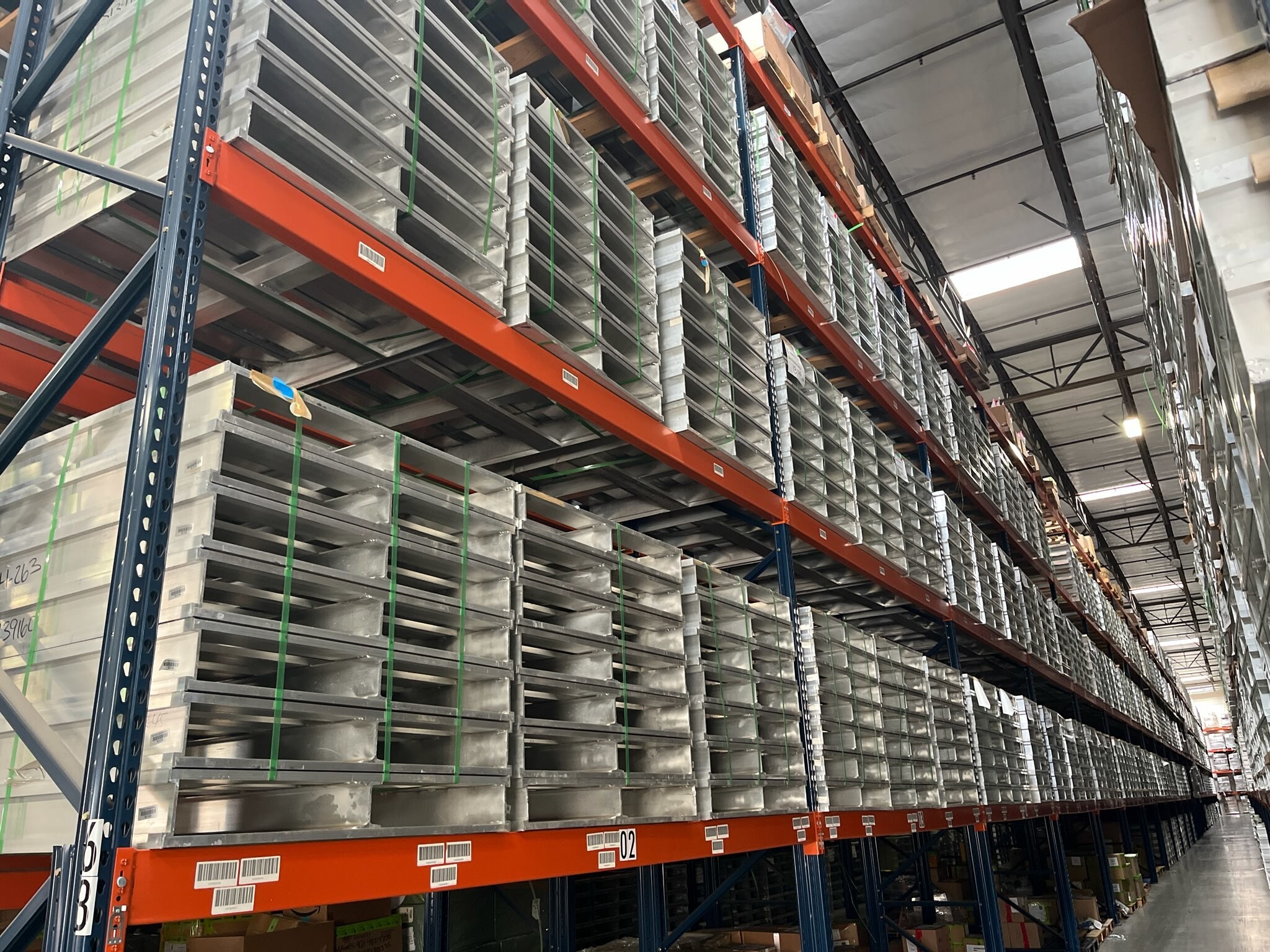 Stacks of aluminum pallets are stored in long, high rows in a warehouse